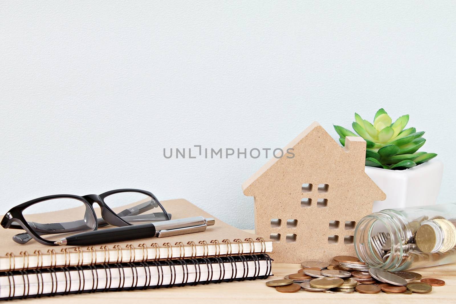 Business, finance, saving money, property loan or mortgage concept :  Wood house model and coins scattered from glass jar on office desk table