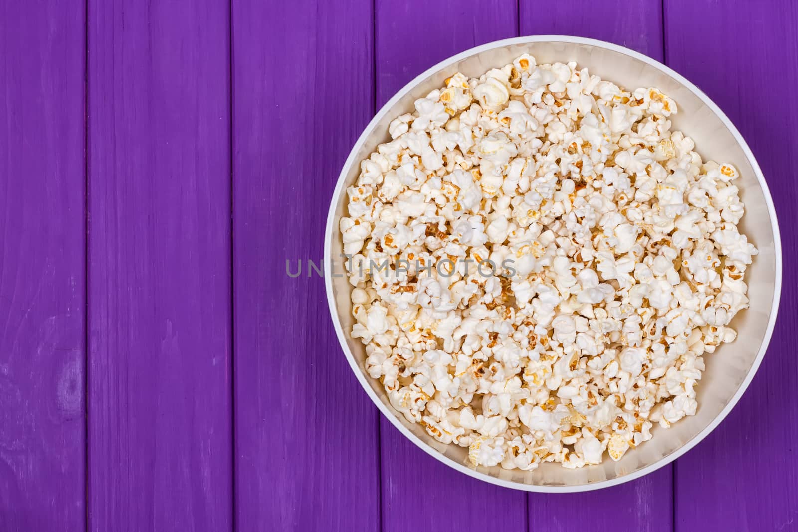 Popcorn in a bowl on purple wooden surface