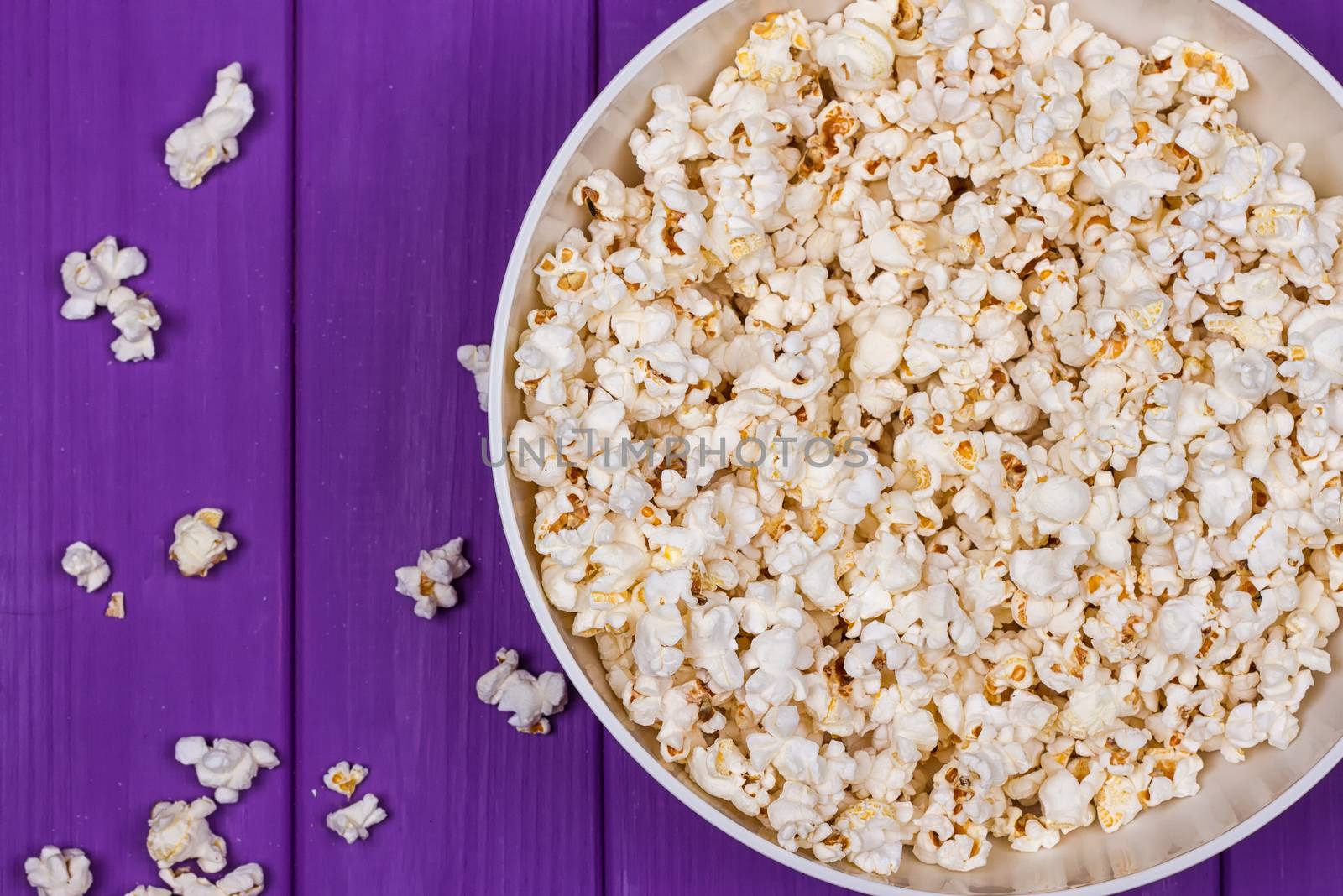 Popcorn in a bowl on purple wooden surface