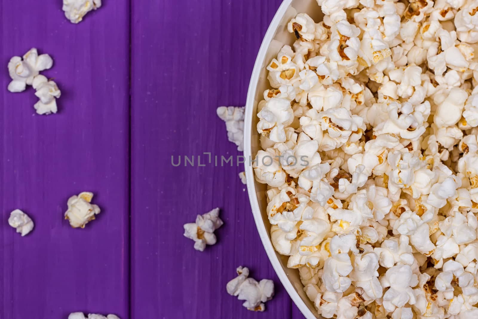 Popcorn in a bowl on purple wooden surface