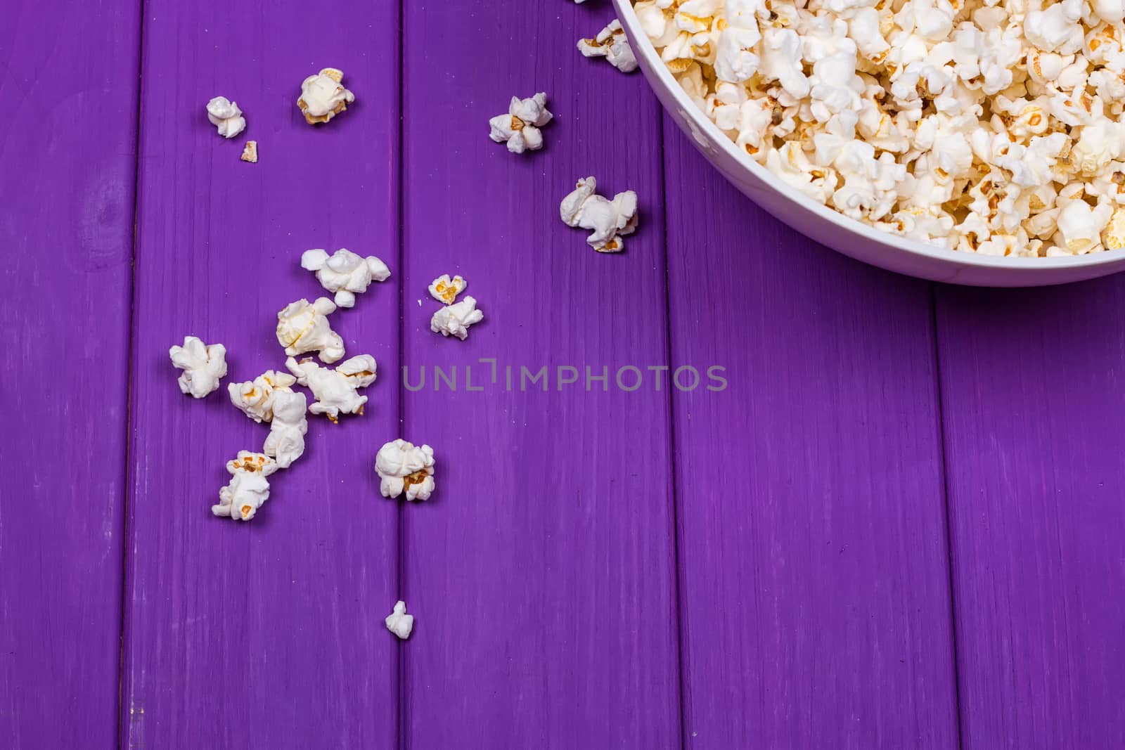 Popcorn in a bowl on purple wooden surface