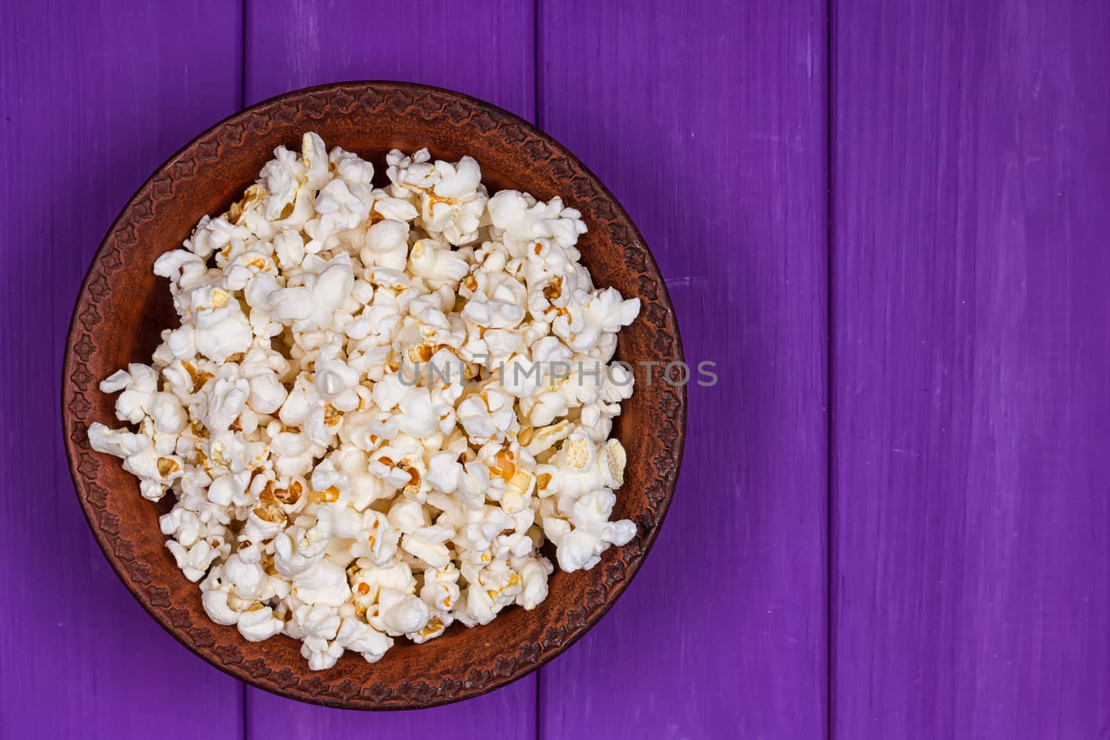 Popcorn in a bowl on purple wooden surface