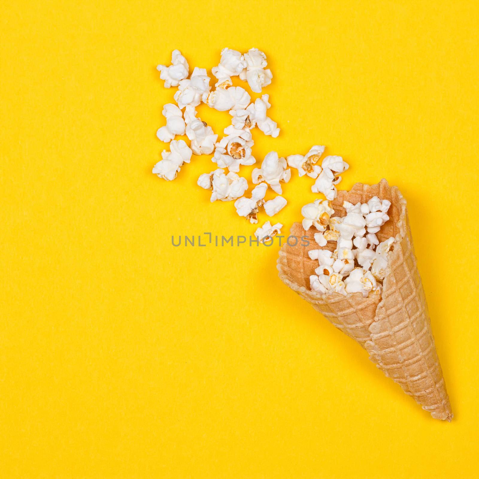 Popcorn in ice cream cones on yellow background. Top view.