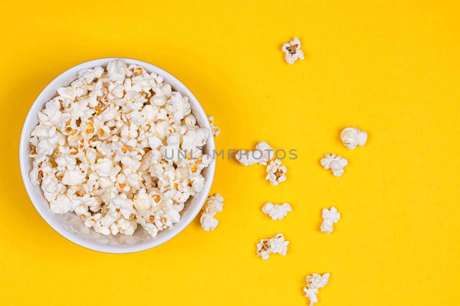 Bowl of Delicious Popcorn spilling onto a yellow background