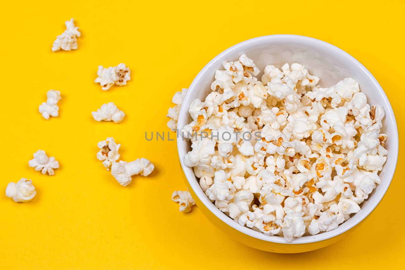 Bowl of Delicious Popcorn spilling onto a yellow background