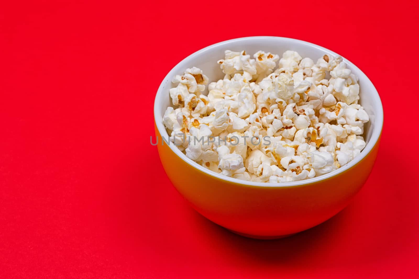 Bowl of Delicious Popcorn spilling onto a red background