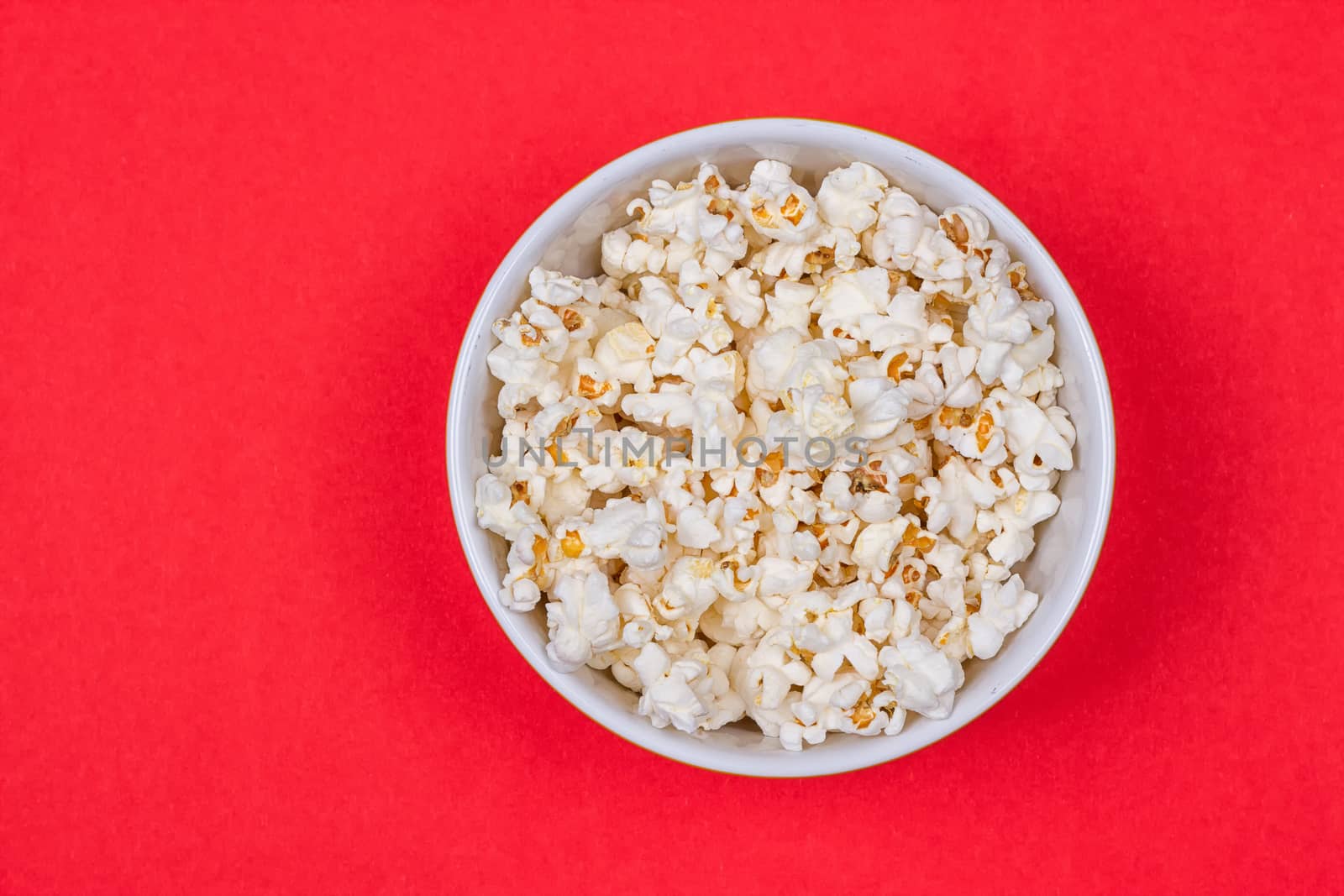 Bowl of Delicious Popcorn spilling onto a red background