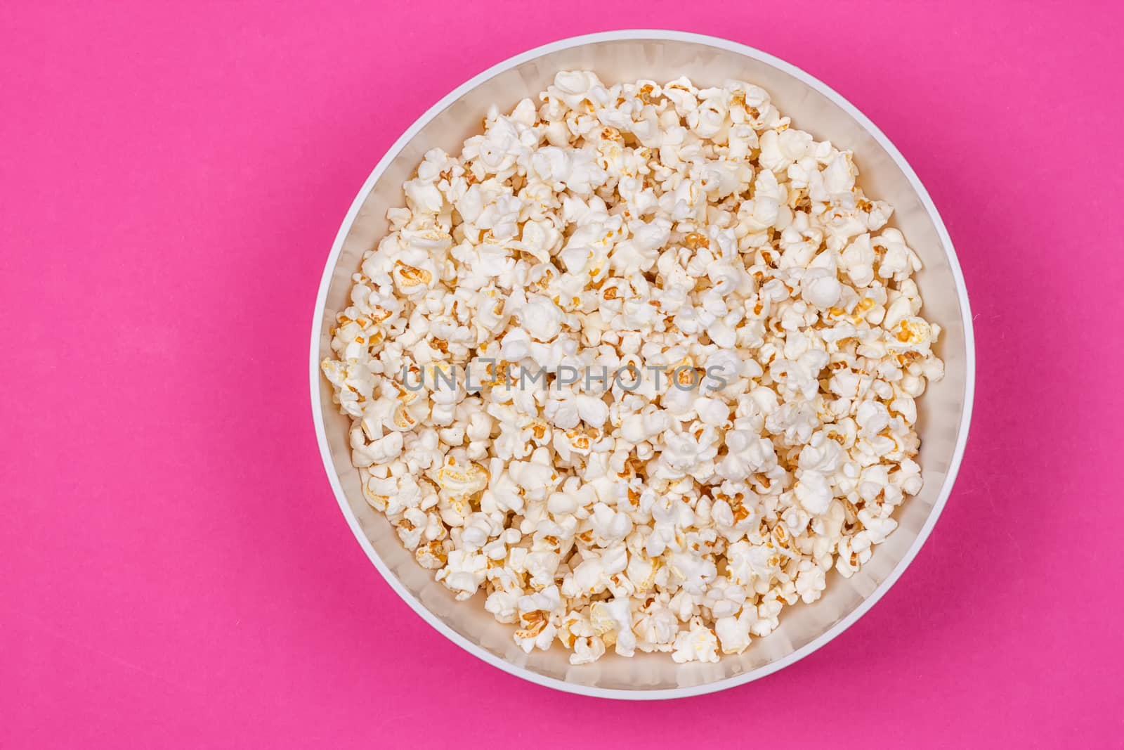 Bowl of Delicious Popcorn spilling onto a pink background