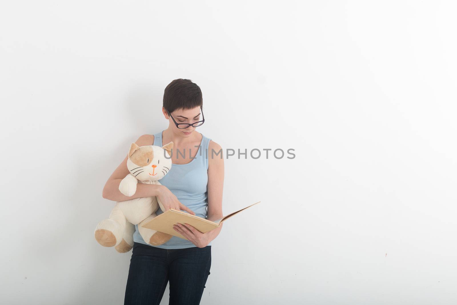 Pretty brunette woman reading book with her plush toy cat. by MSharova