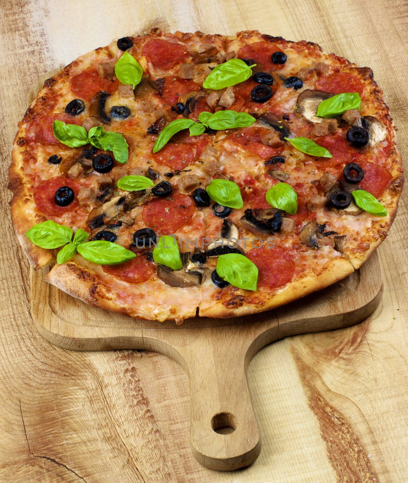 Homemade Pepperoni Pizza with Black Olives, Mushrooms, Ham and Basil Leafs on Wooden Cutting Board closeup on Wooden background