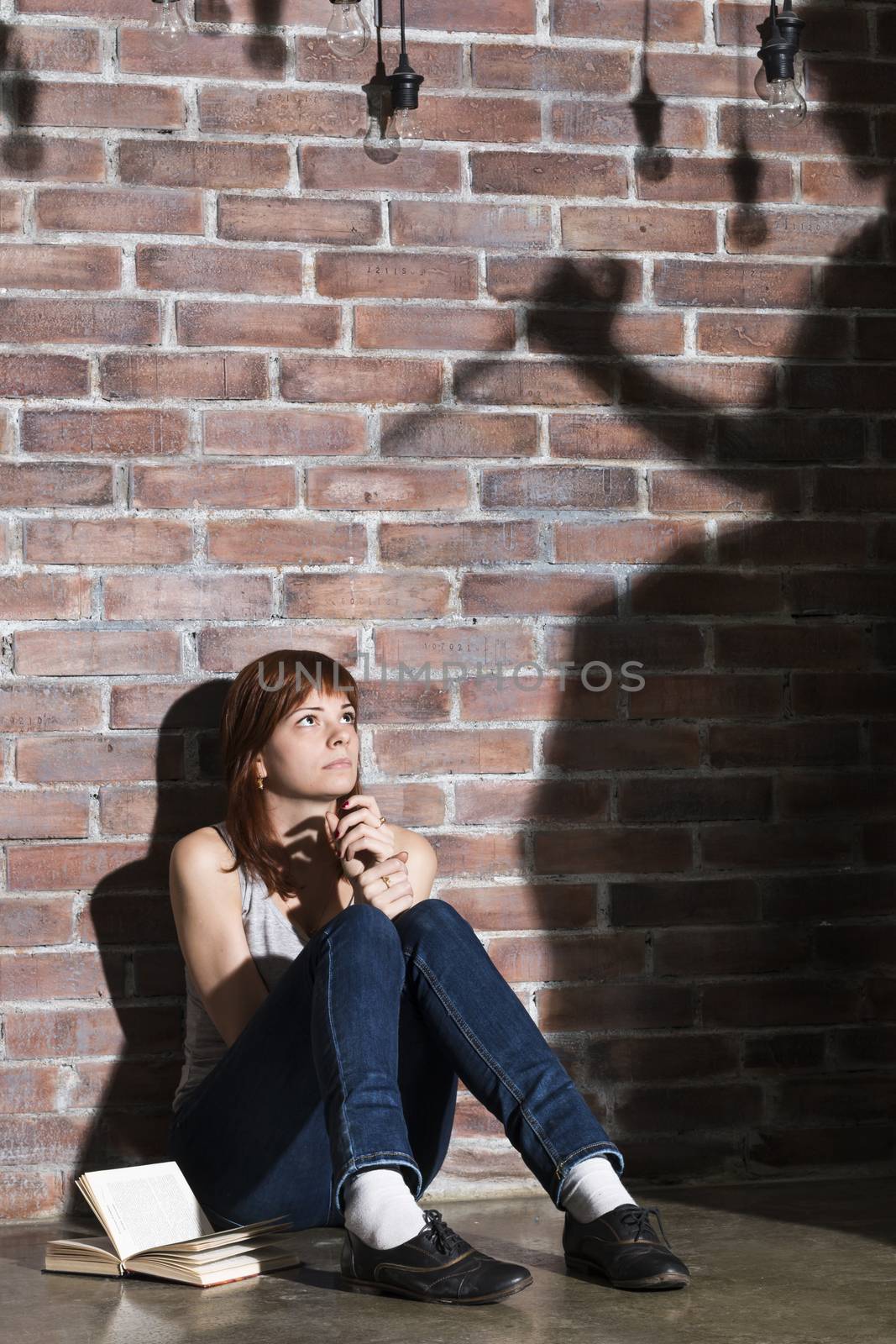 Caucasian girl sitting on the floor reading a horror or scary thriller book. Dramatic lighting with girls eyes wide open and long shadows of woman with knife on the wall near her. Terrified expression by MSharova