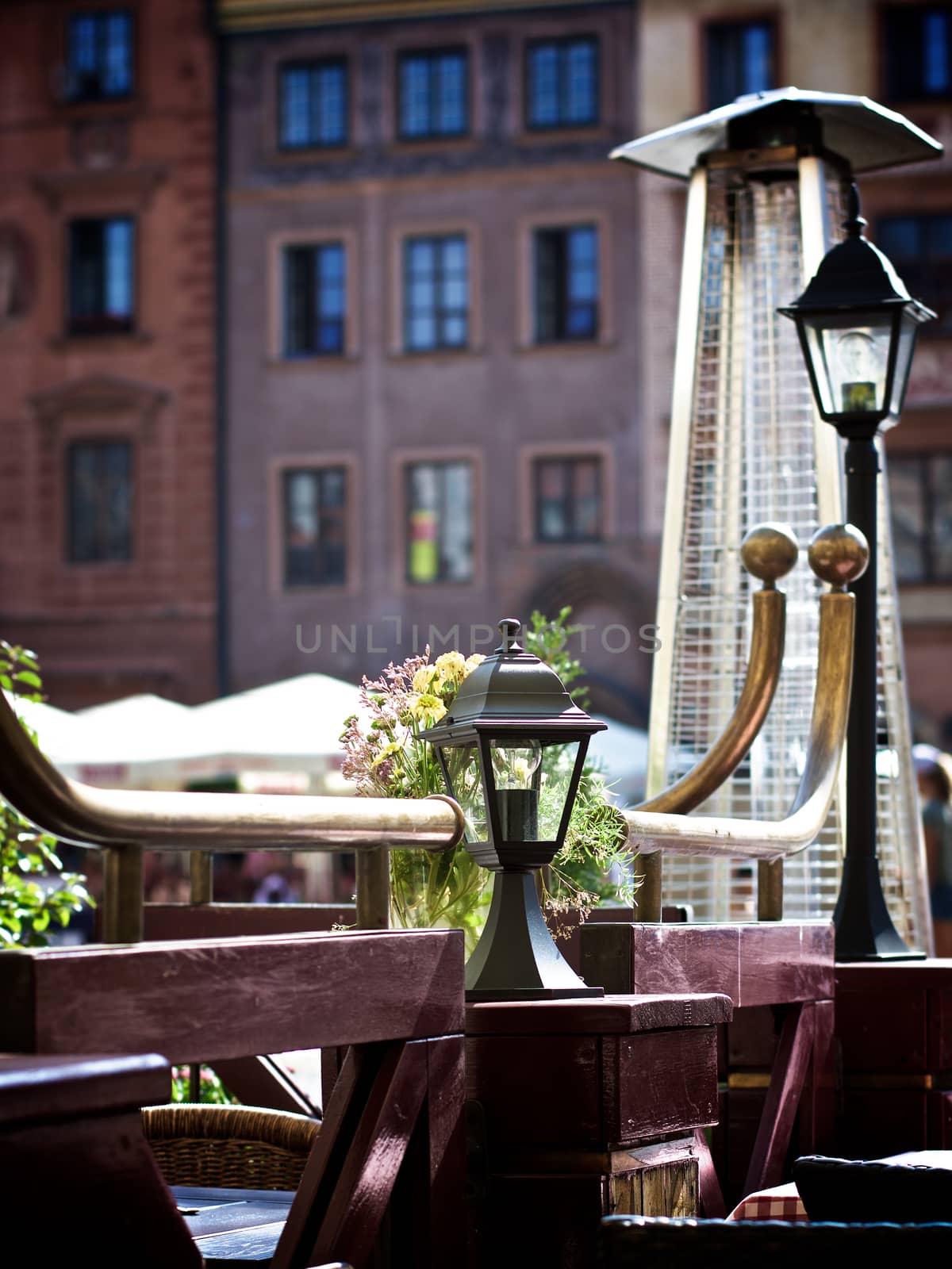 Old Empty Sidewalk Cafe with Wooden Tables, Partitions, Street Lanterns and Heat Stands against Blurred Medieval Houses Outdoors. Warsaw, Poland