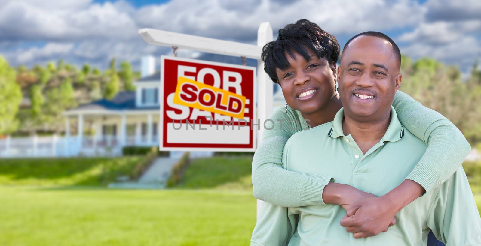 Happy African American Couple In Front of Beautiful House and Sold For Sale Real Estate Sign.