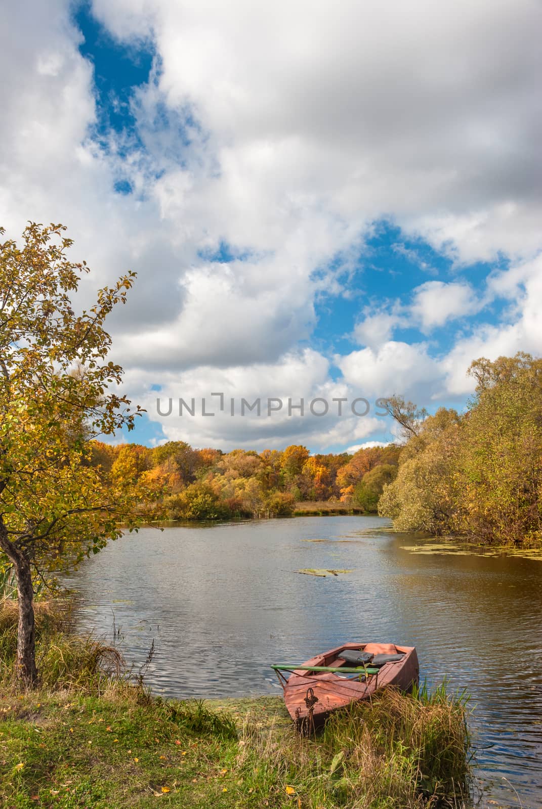 Beautiful autumn landscape with old boat on the riverbank against a forest