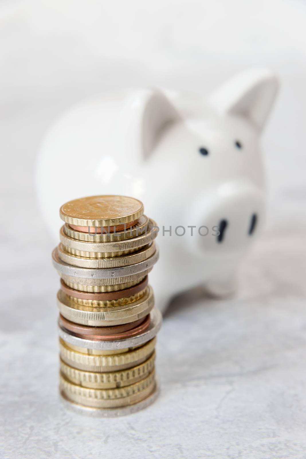 Concept of investing or saving: white ceramic piggy bank and a tower of euro coins