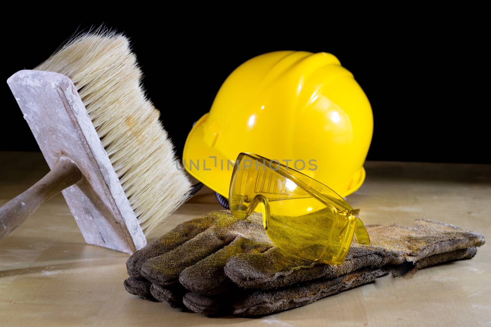 Safety glasses, helmet, work gloves and brush. Tools on a wooden table. Black background.