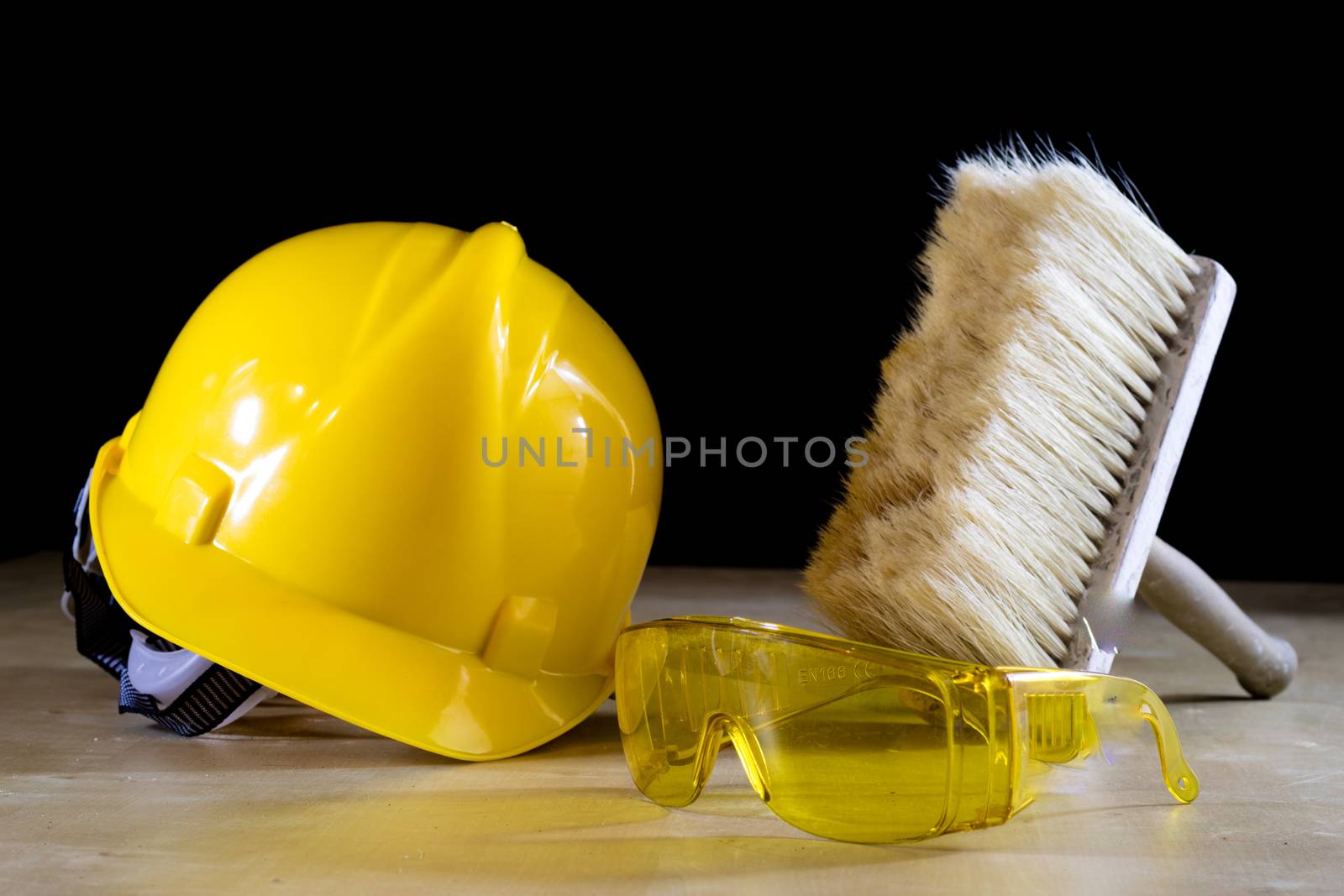 Safety glasses, helmet, work gloves and brush. Tools on a wooden table. Black background.