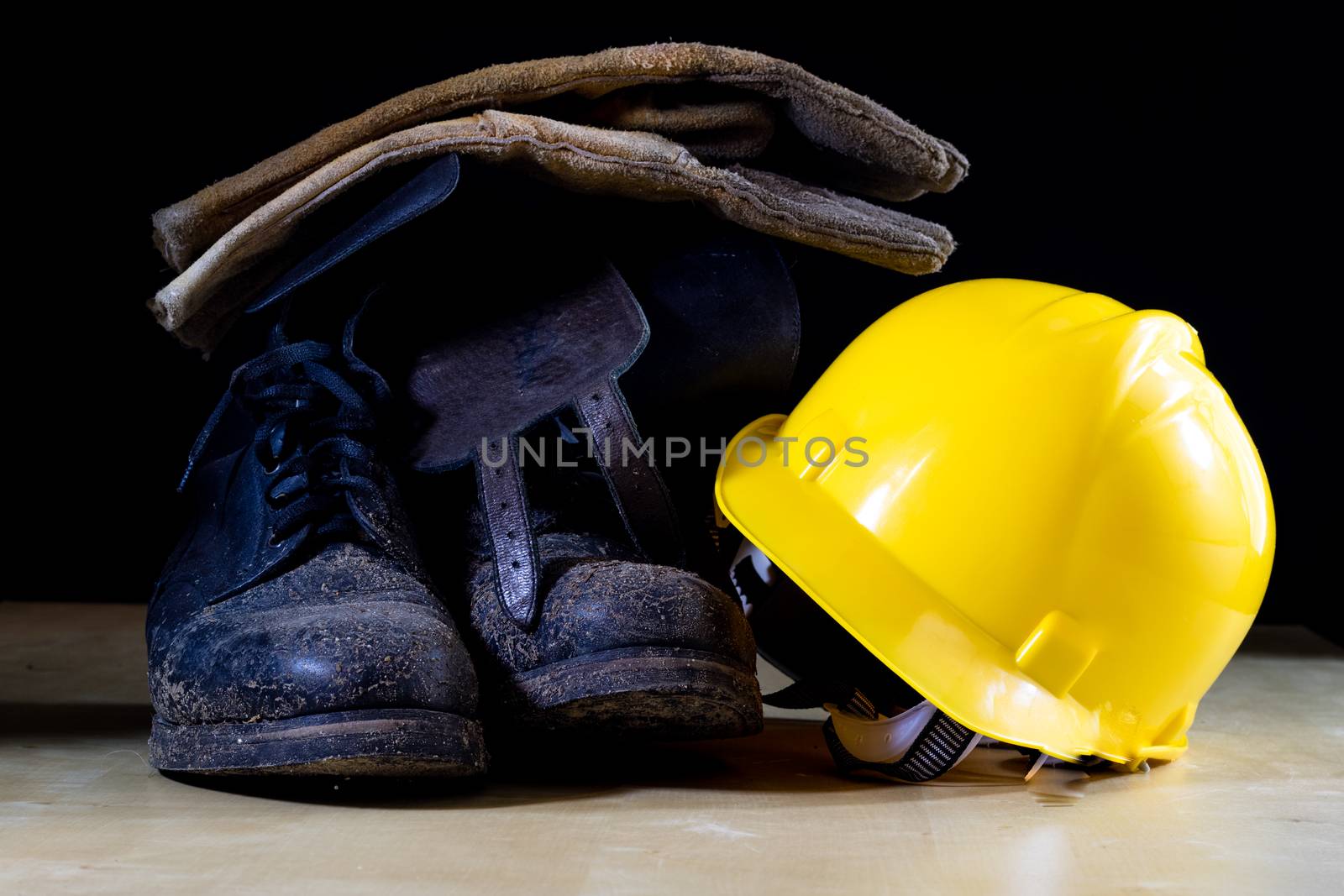 Muddy working boots with helmet and gloves. Accessories for the worker. Black background.