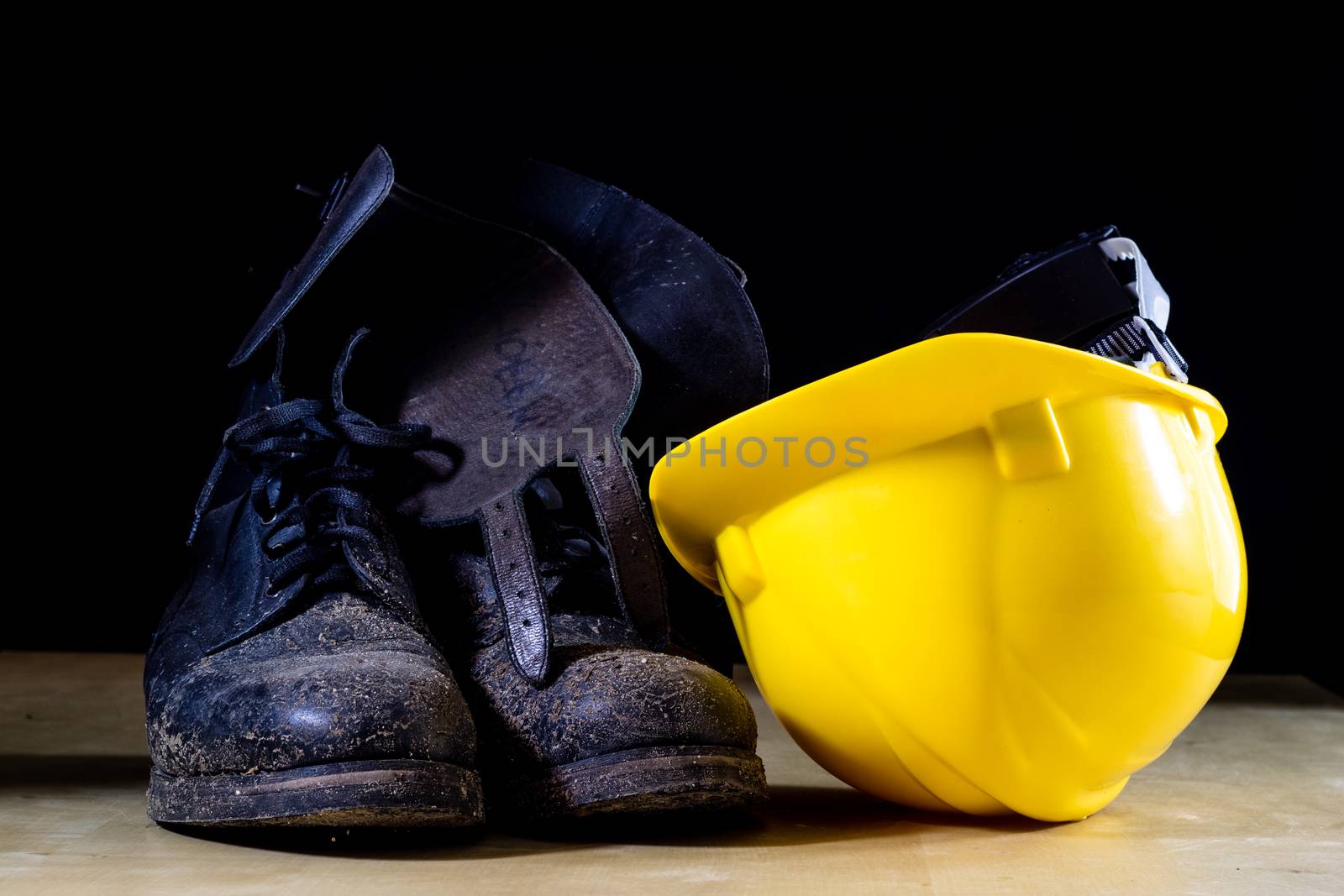 Muddy working boots with helmet and gloves. Accessories for the worker. Black background.