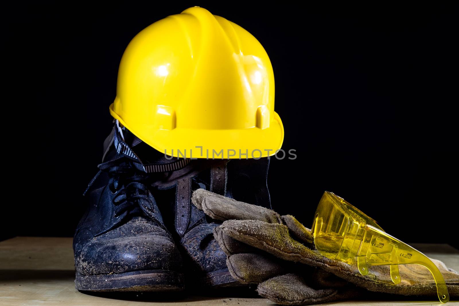 Workwear for a construction worker. Helmet, gloves, shoes and sunglasses on a wooden table. Black background.
