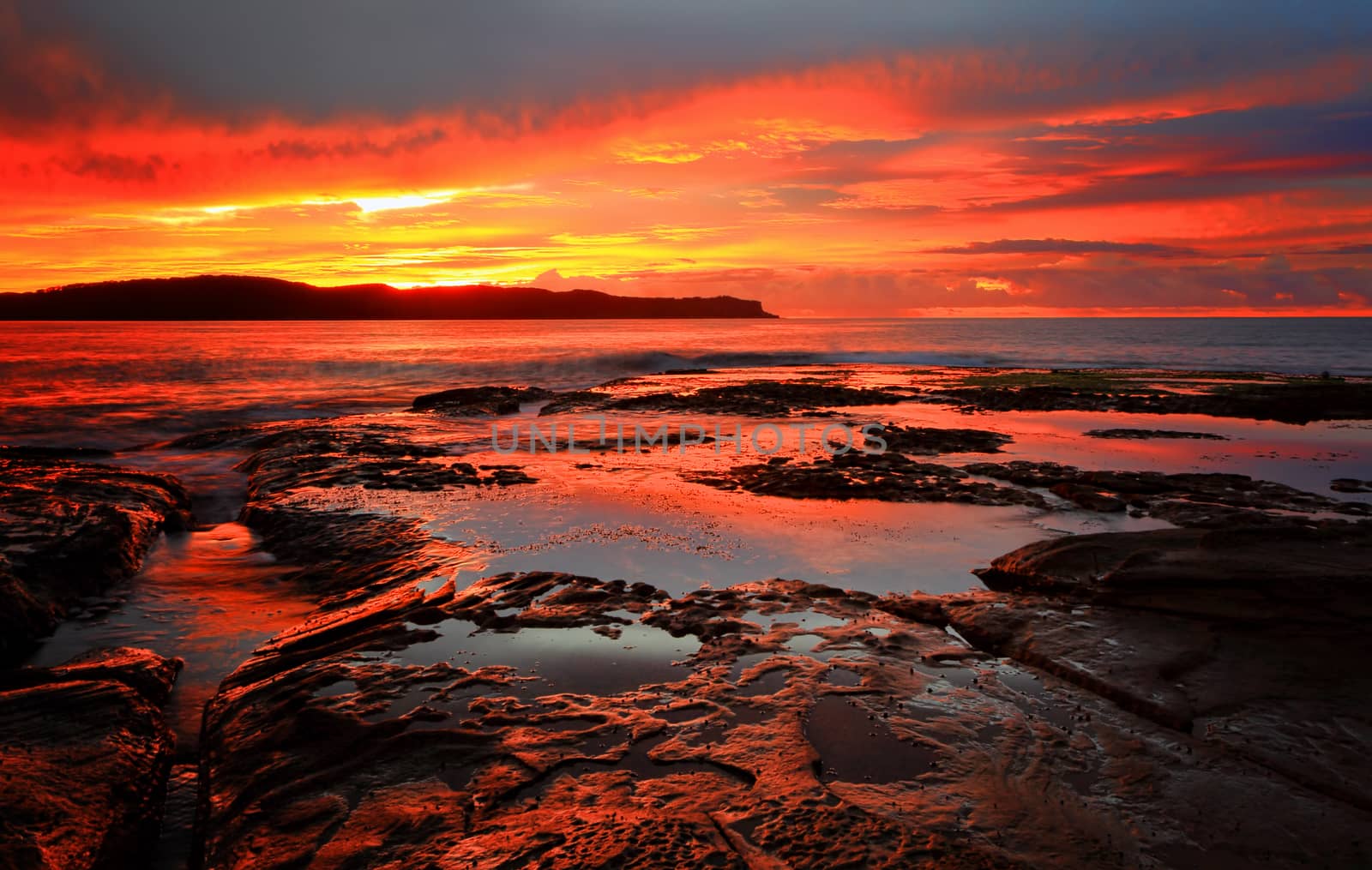 Rich red velvet sunrise casts its hues over Pearl Beach, the ocean and the rocks and rock pools in the foreground