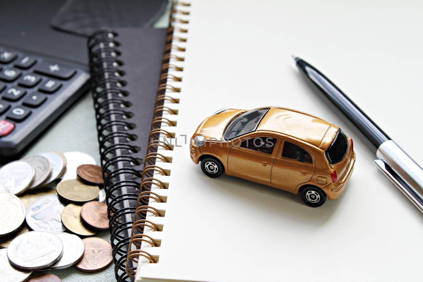 Business, finance, saving money, banking or car loan concept : Miniature car model, pen, notebook papers, calculator and coins on office table