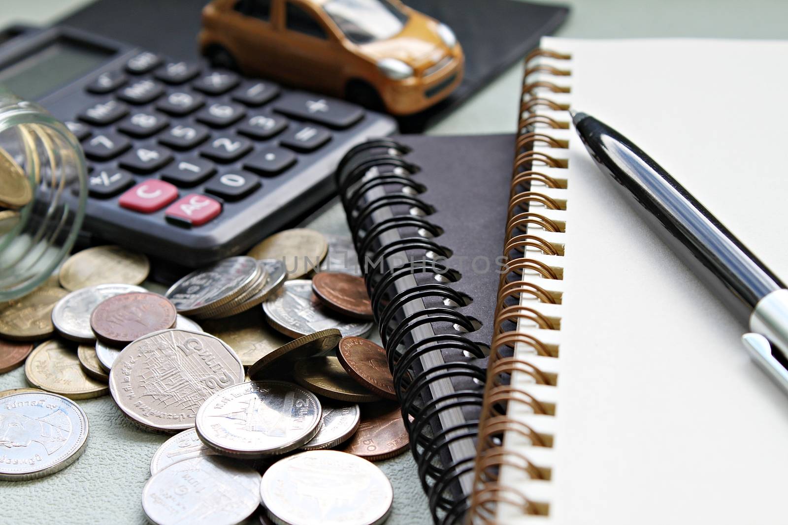 Business, finance, saving money, banking or car loan concept : Miniature car model, calculator, coins scattered from glass jar, notebook paper and pen on office desk table