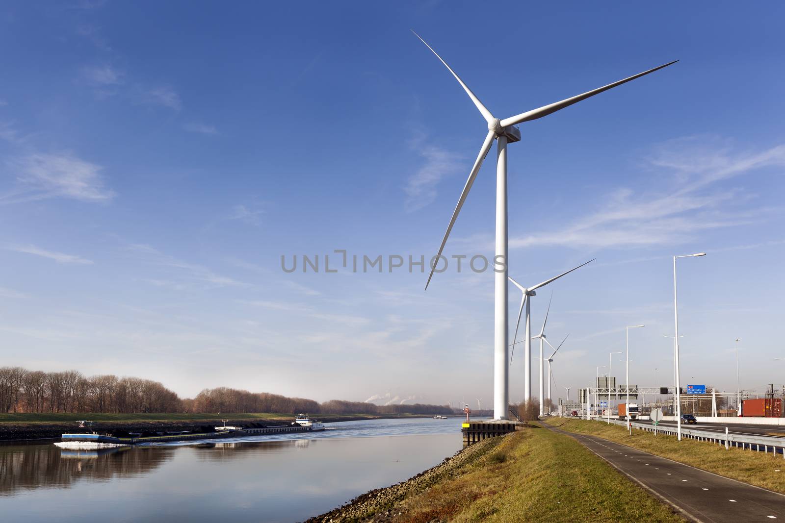 Wind turbines near canal Hartel and a ship loaded with charcoal in industrial area Europoort of Rotterdam in the Netherlands