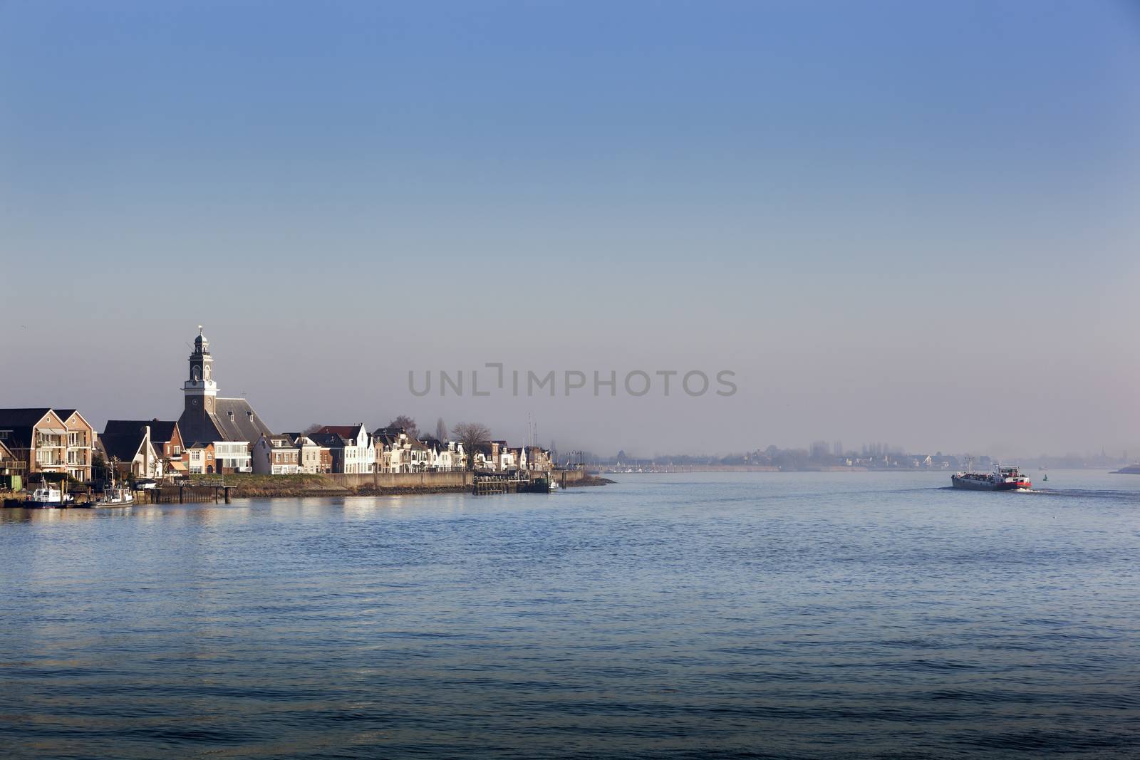 Village Lekkerkerk near the river Lek in the Netherlands. An industrial  ship is passing by.