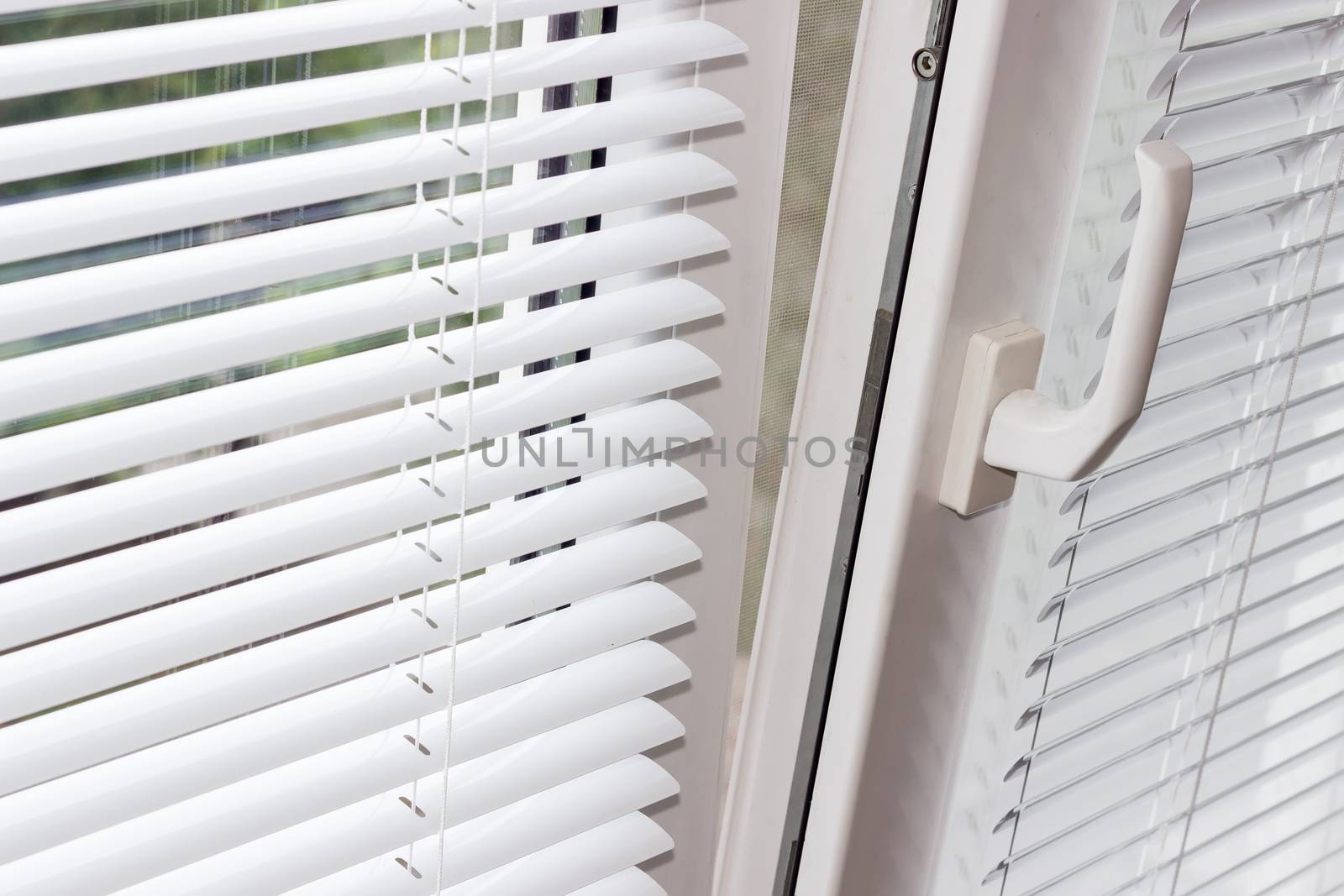 Fragment of the modern tilt and turn plastic window tilted inwards at the top with control handle and white Venetian blinds 
