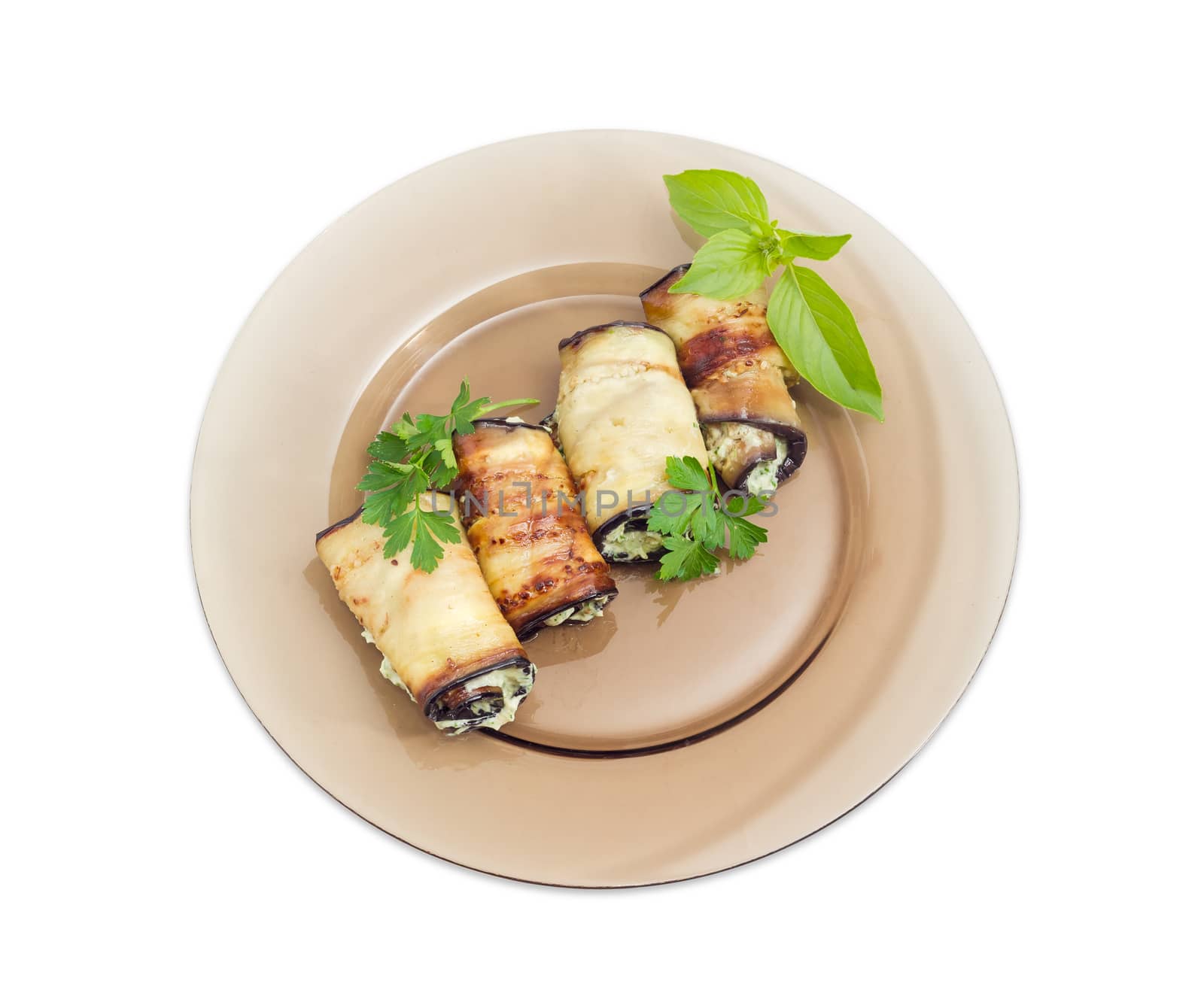 Top view of a dark glass dish with several eggplant rolls stuffed with tuna and processed cheese and decorated with parsley and basil twigs on a white background 
