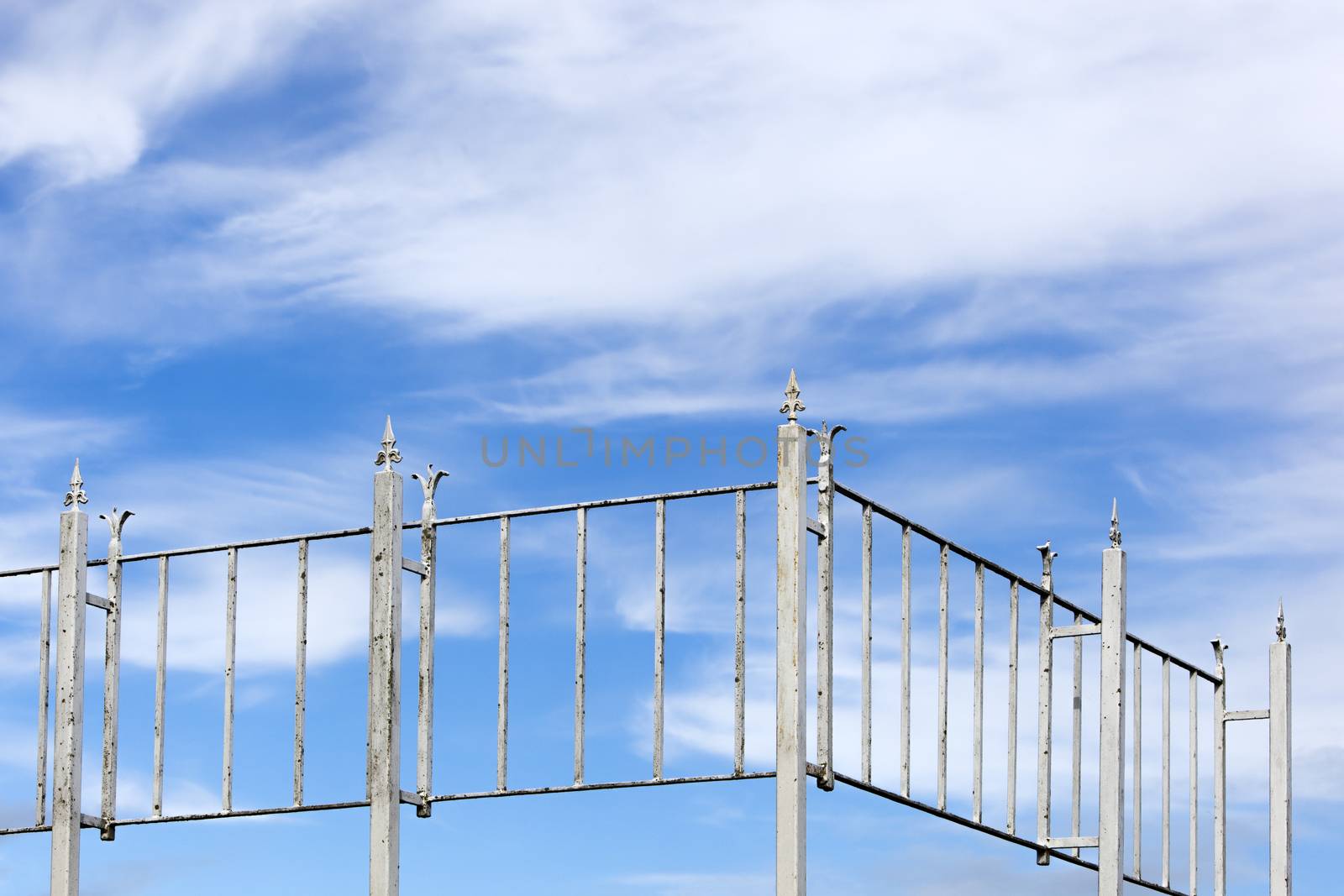 Vintage rusty white metal fence and a blue cloudy sky