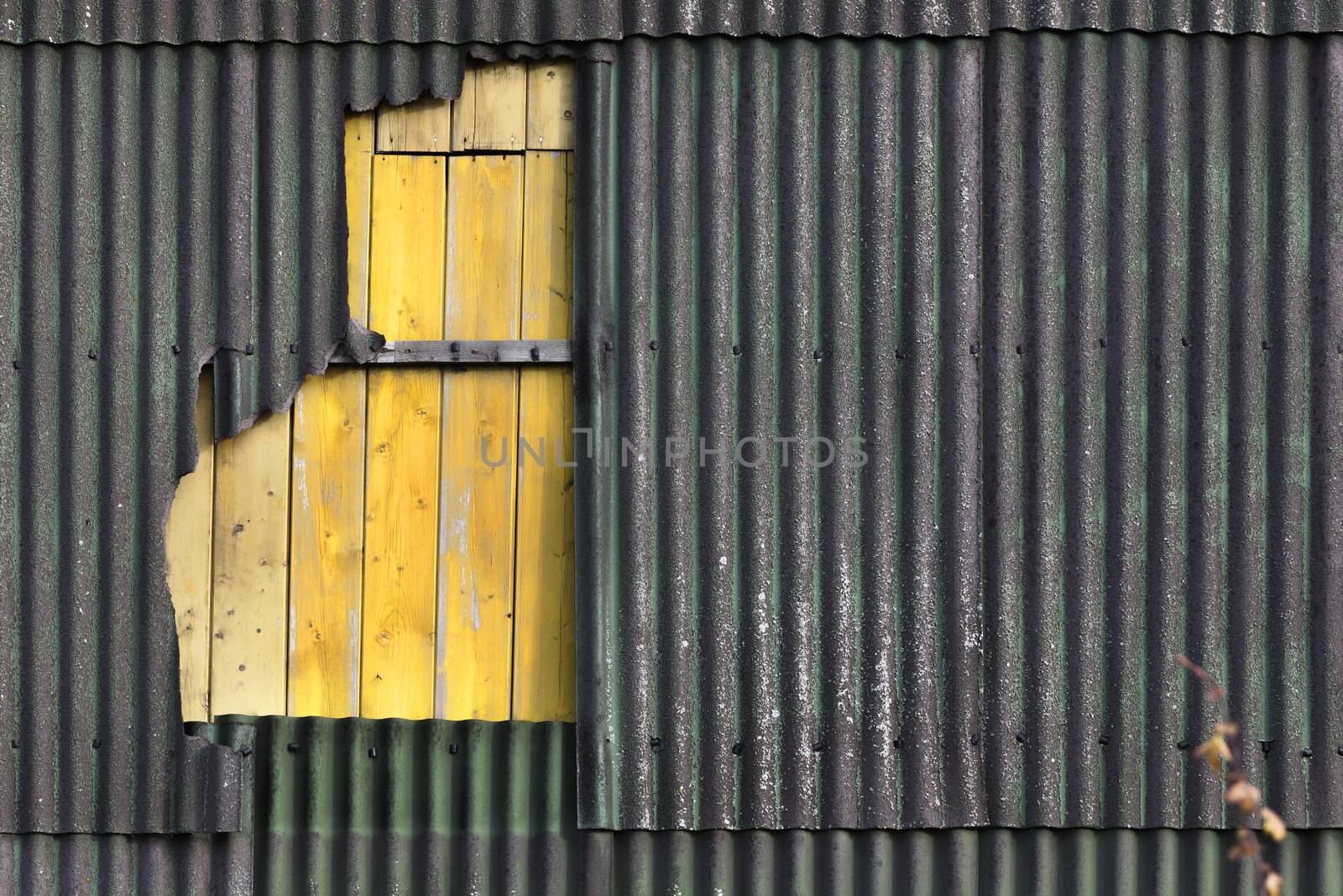 Old damaged wall of corrugated asbestos material repaired with yellow timber