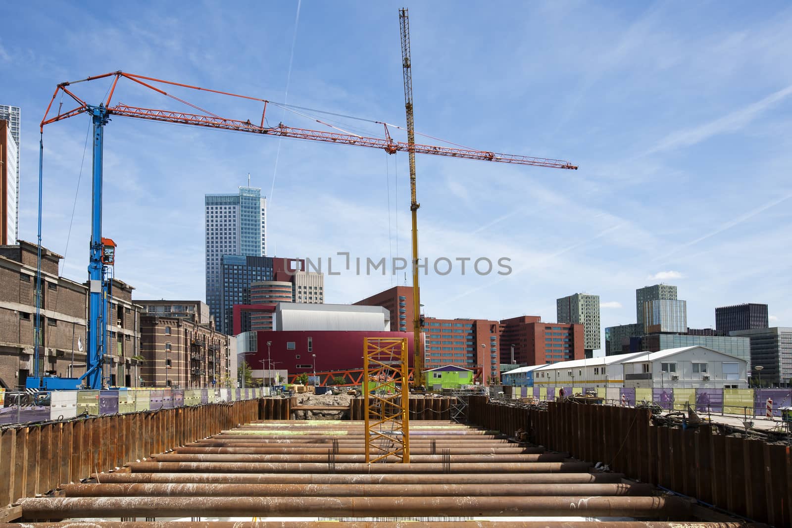 Construction site with 2 cranes in Rotterdam, in the Netherlands. Modern architecture and old warehouses in the background.