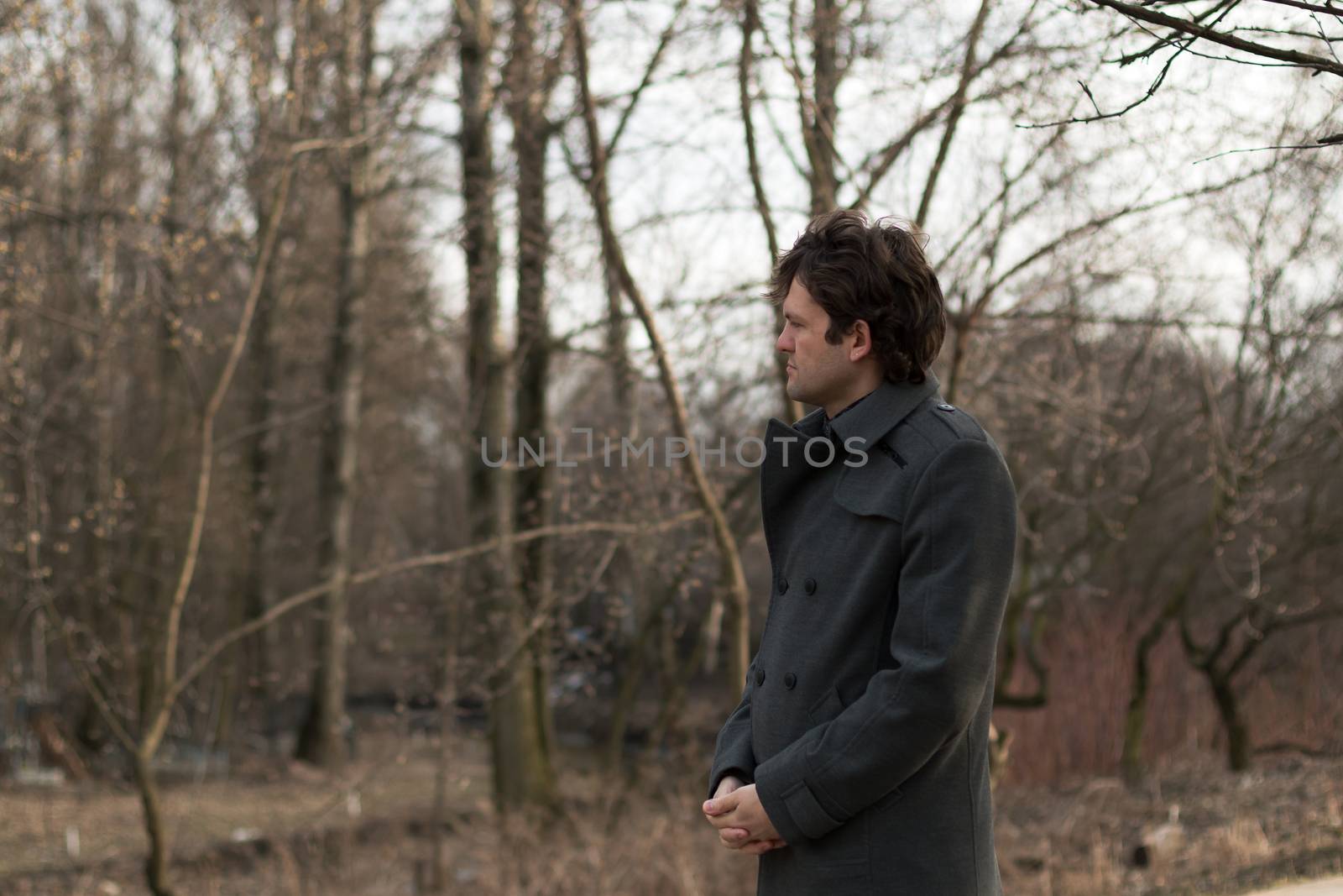 Portrait of a young handsome man sad looking to the left in the park, the woods in autumn or spring. Portrait on the nature of the park, the woods, on the street, horizontal picture. Real people series