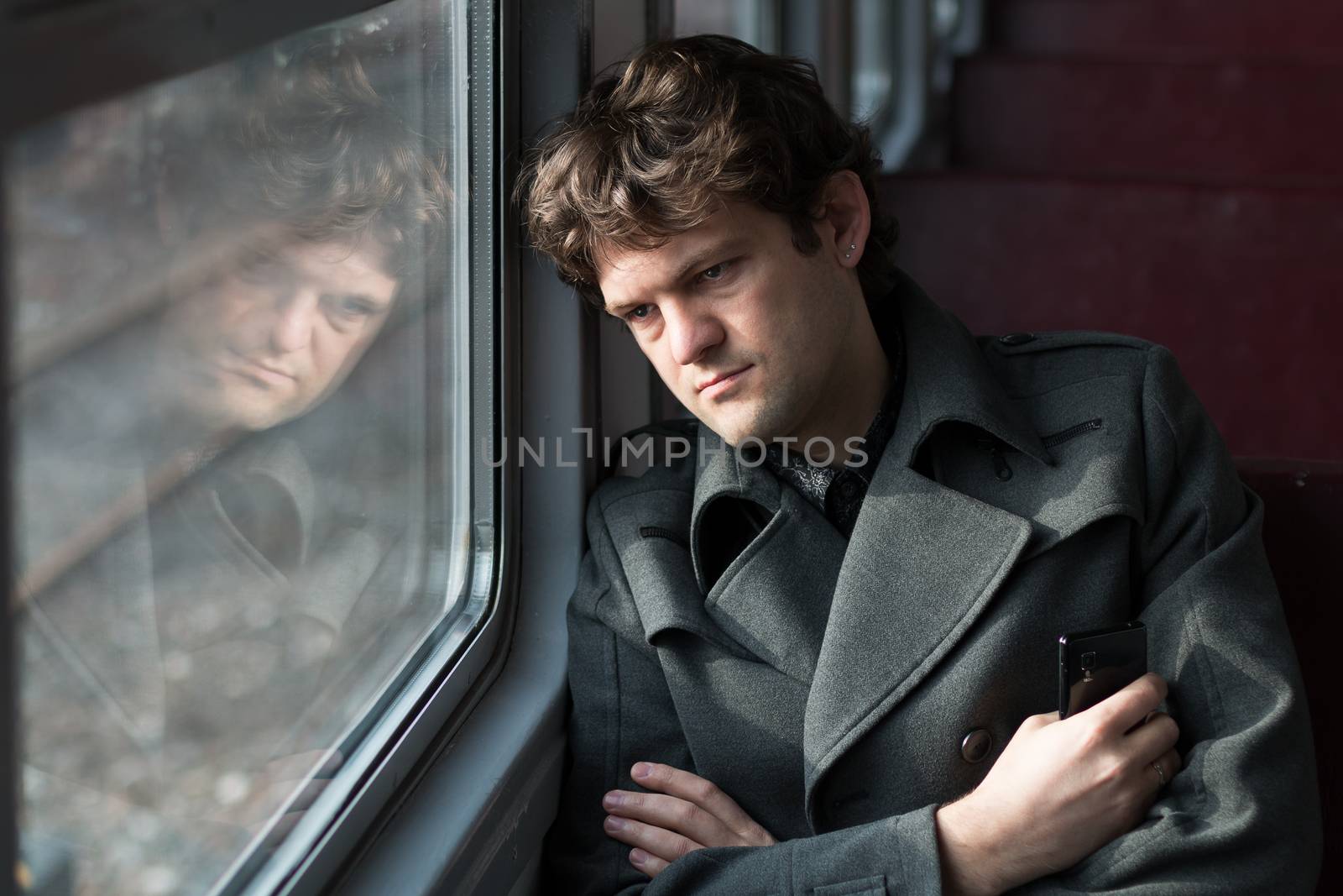 Traveling by train. Sad man traveling by train, looking through the window and thinking about unrequited love squeezing the phone in his hand. alone in an empty train wagon. Real people series. Toned picture.