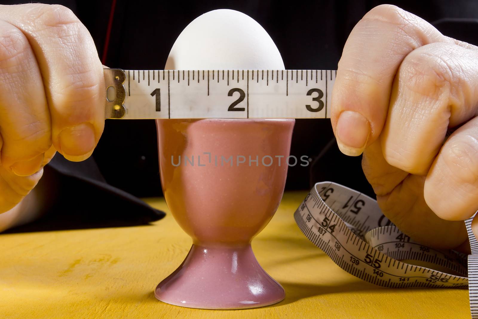 Egg in the holder and hands of the cook with a tape measure