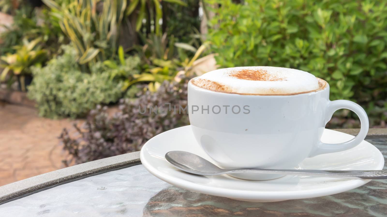 Closeup A cup of hot cappuccino on glass table with garden nature background