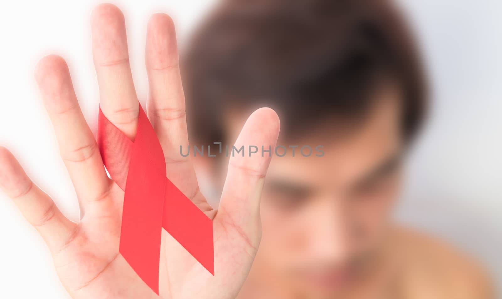 Hand hold red ribbon with blurred effect man background for AIDs awareness concept