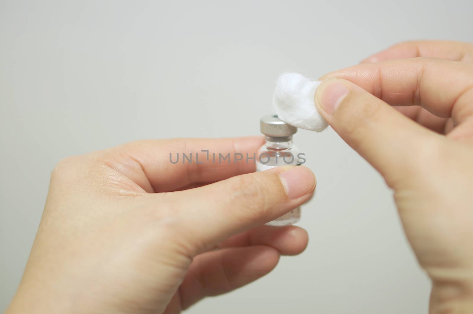 Hand of nurse is cleansing vial vaccine by cotton ball with alcohol for injecting vaccine with white background.