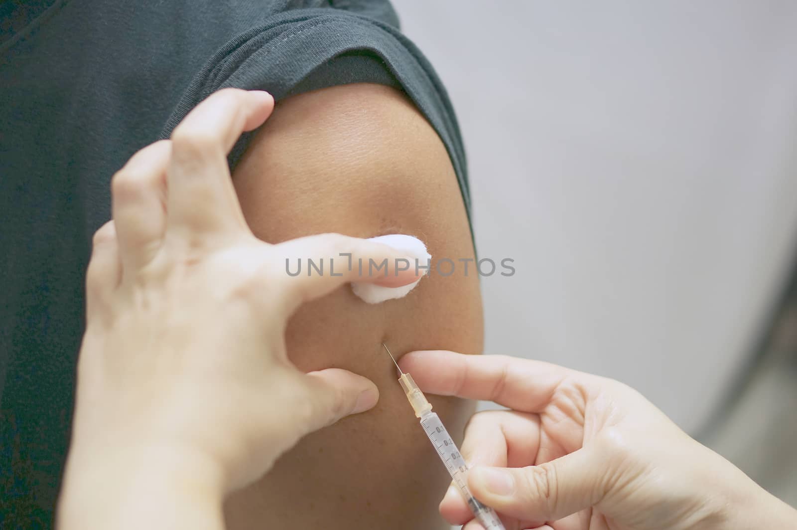 Hand of nurse holding hypodermic syringe and cotton ball is injecting vaccine with patient man in black T-shirt.