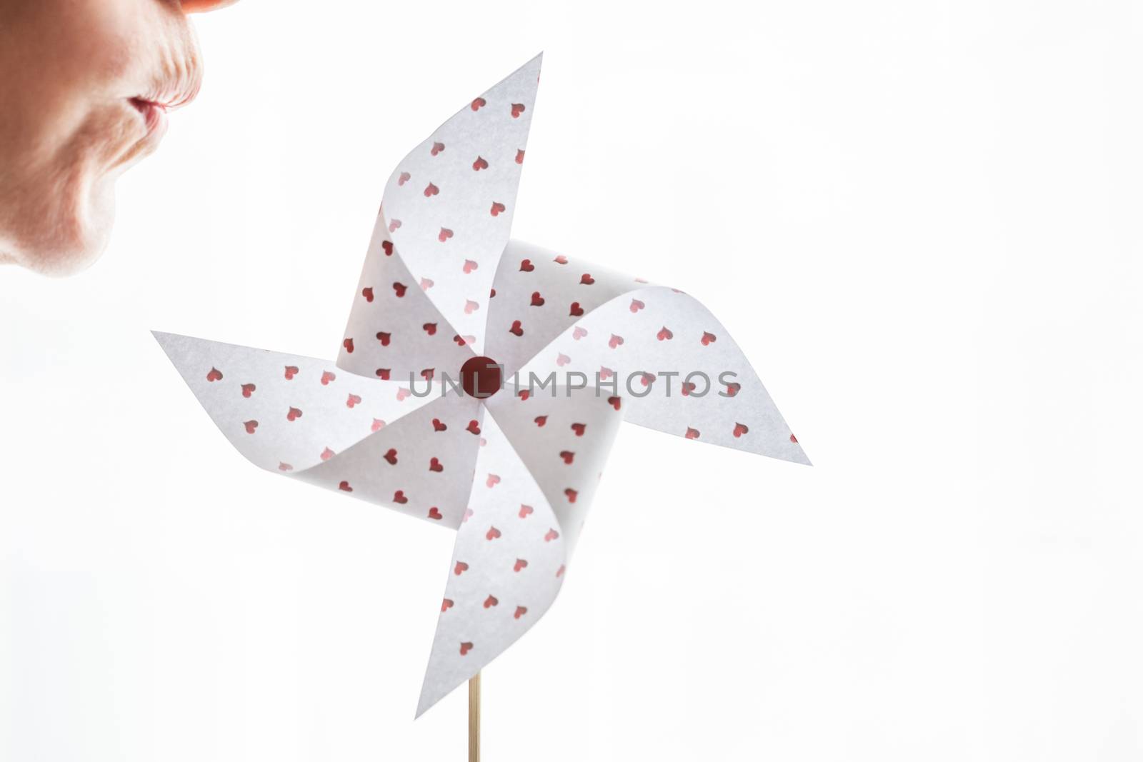 Woman blowing a hearts paper pinwheel isolated on white background