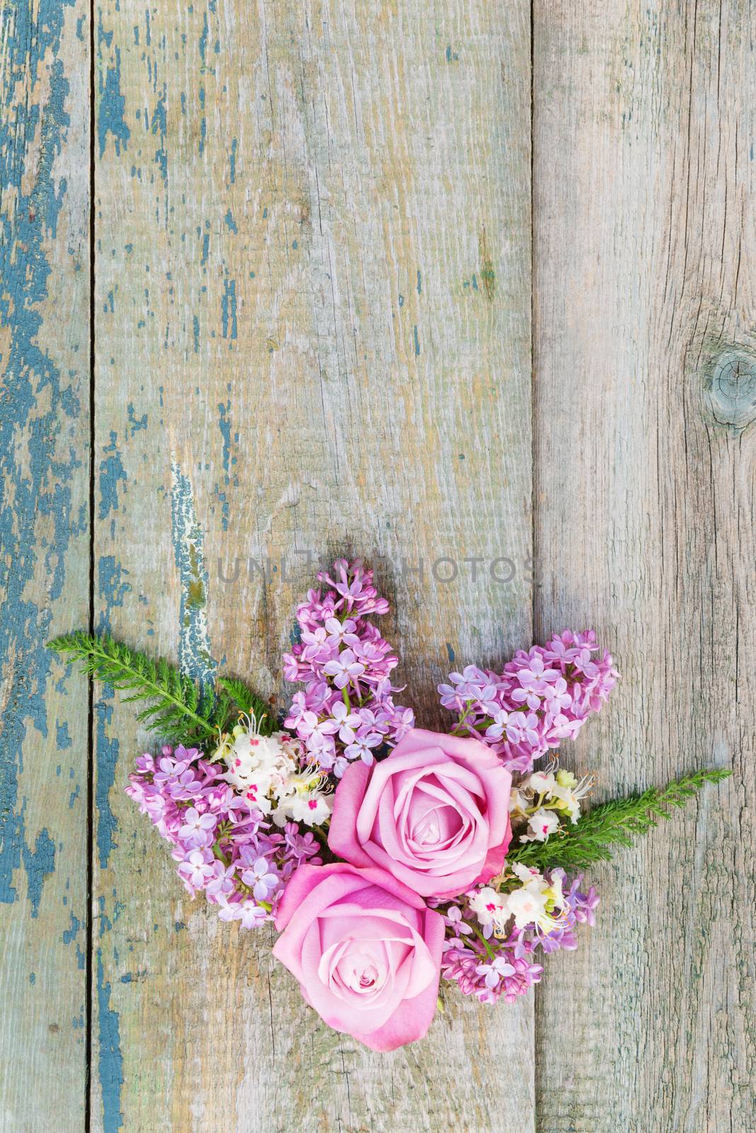 Decorative composition consisting of pink roses, violet lilac flowers and green leaves on the old wooden background. Flat lay, top view, with copy-spase