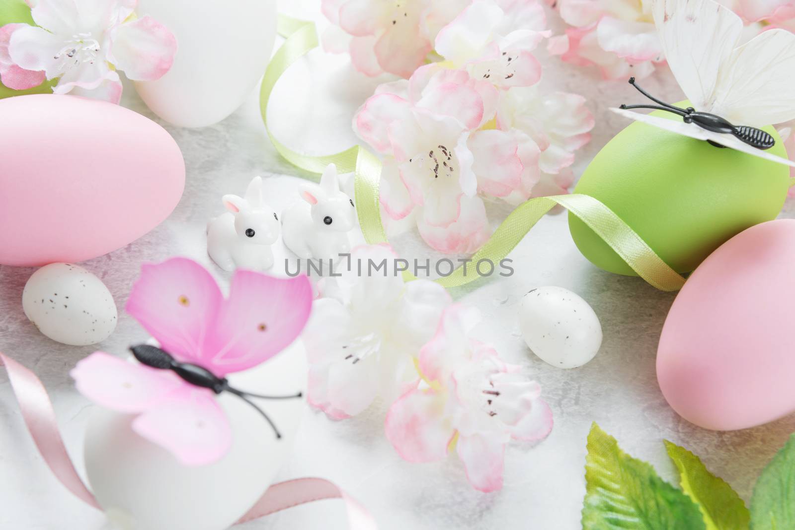 Beautiful delicate Easter composition with pink cherry flowers, multicolored Easter eggs, Easter bunny and butterfly on the stone background