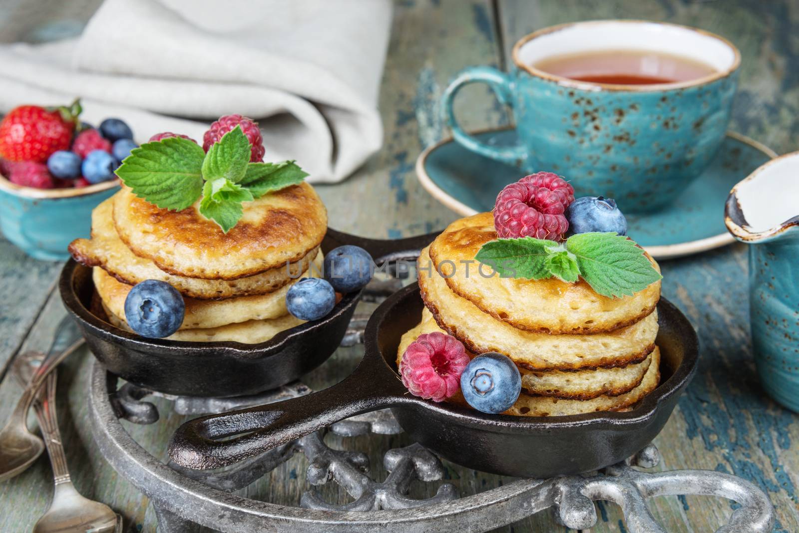 Breakfast of pancakes in cast-iron frying pans, fresh berries and black tea, in rustic style