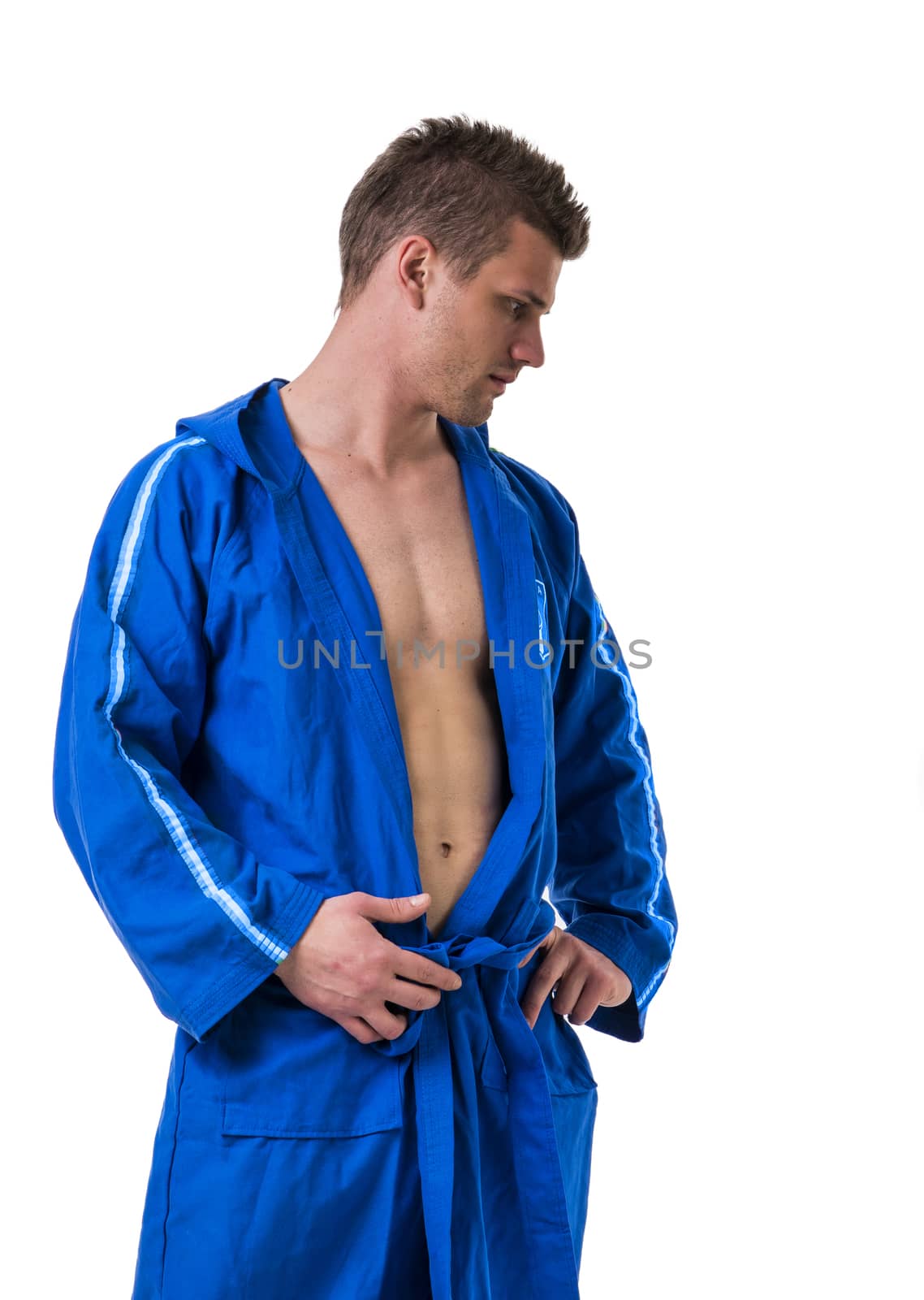 Handsome young man wearing blue bathrobe, looking down, isolated on white background