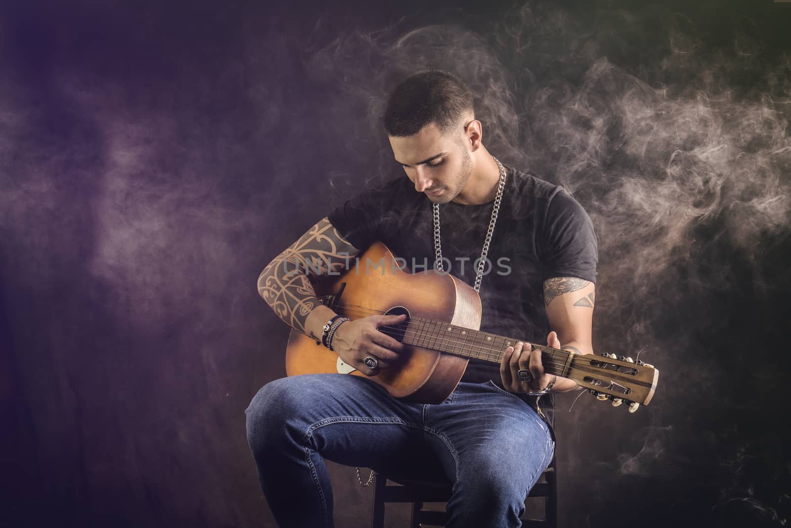 Portrait of hipster playing guitar against black background, in studio shot