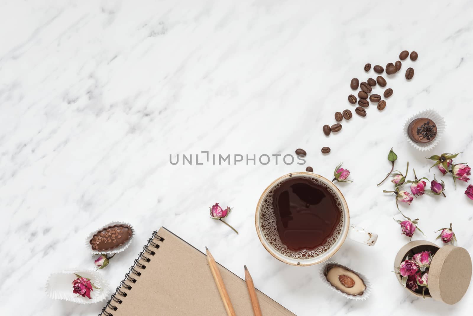 Morning composition with a cup of black coffee, chocolate candies and a notebook on a marble surface with space for text, top view