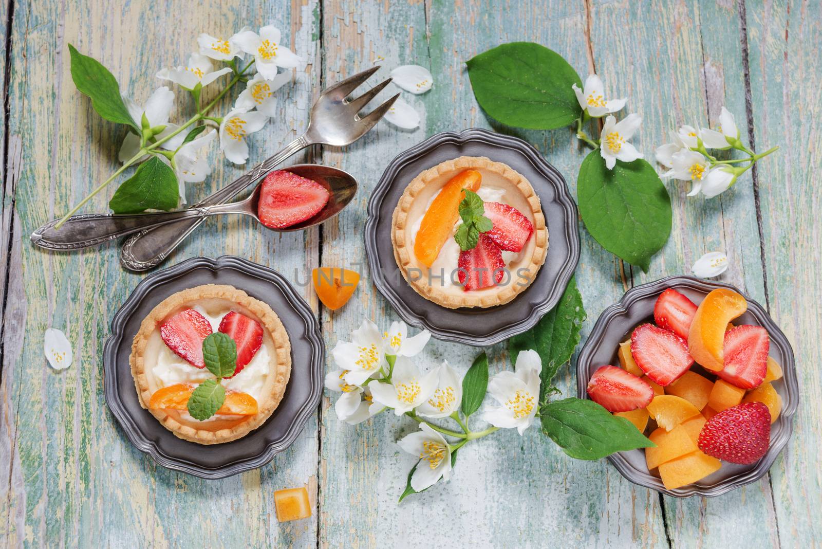 Still life with tartlets filled with cream and berries and jasmine flowers on old shabby boards, top view