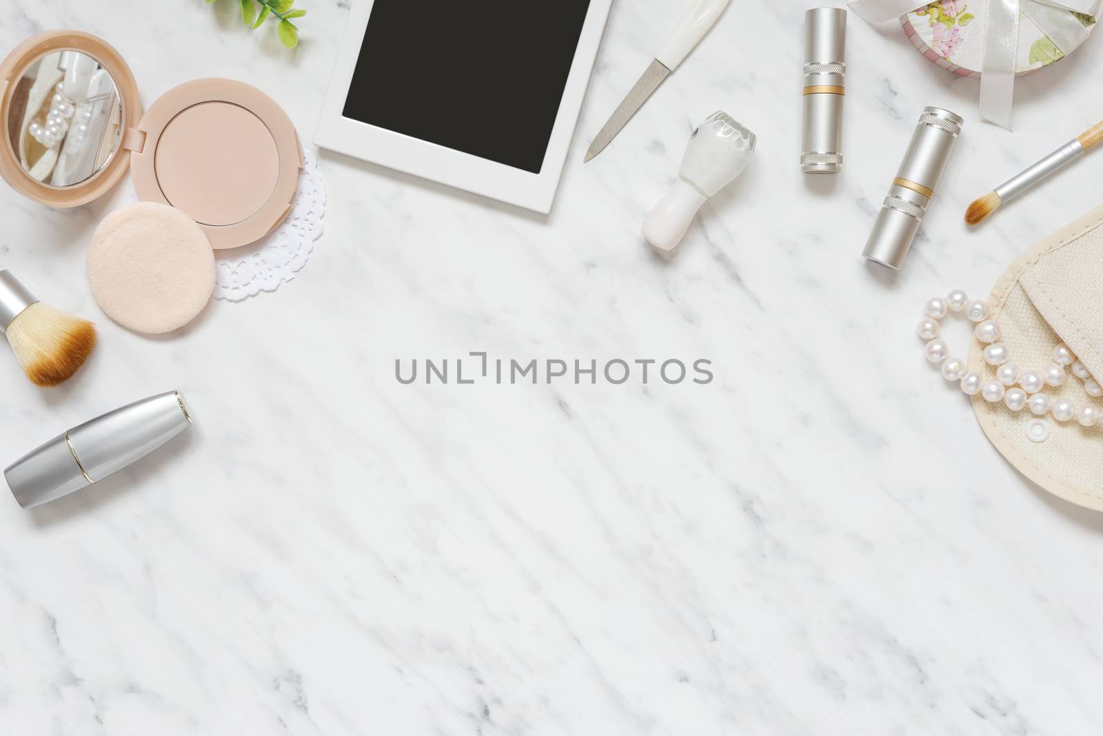 Feminine workspace on table desk with smartphone, lipstick; pearl necklace, compact powder, cosmetic brushes and nail polish on marble stone background; top view, flat lay